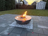Reflective water surface of a 40-inch travertine 360 fire and water bowl on a modern grey stone patio.