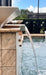 Travertine TessaRai Square Fire/Water Bowl Kit side view with cascading spillway on luxury backyard pool wall