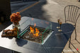 Functional detail of the Brugge Bulgaria Black dining fire table used for outdoor meals, with the burner lid in place and styled with wine, champagne, and a fruit tray.