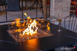 Close-up of the Brugge Bulgaria Black dining table’s linear burner, highlighting the clear glass wind guard and bronze-tinted fire glass reflecting a warm flame.