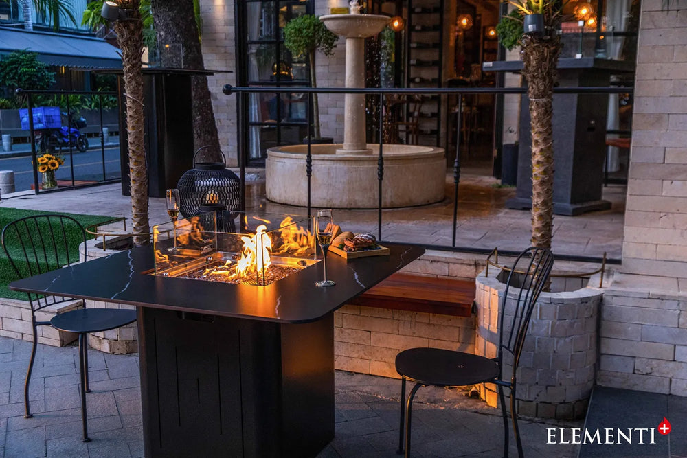 Elementi Plus OFP202BB Brugge Bulgaria Black dining fire table with a dark charcoal porcelain top, styled in a luxury patio setting with white modern chairs.