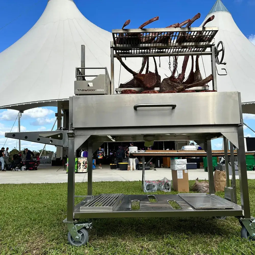 Tagwood BBQ23SS XL Santa Maria grill cooking large tomahawk steaks at outdoor BBQ event
