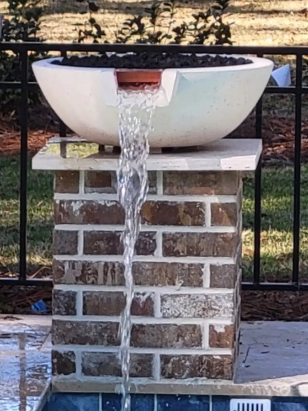 White Travertine TessaRai fire and water bowl with copper scupper spillway mounted on brick pool pedestal.