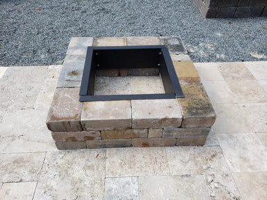 Construction and assembly phase of a Travertine TessaRai square fire pit kit showing the base stone block layout and steel liner insert on a travertine tile patio.