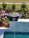 Travertine TessaRai fire and water bowl with clear fire glass and waterfall feature above resort-style pool.
