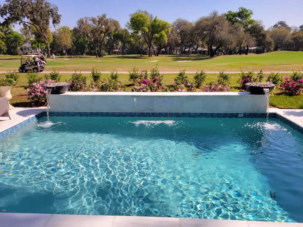 Pair of Travertine TessaRai fire and water bowls with spillways overlooking backyard pool and golf course view.