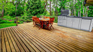 Sunstone SCPBAYOU8.6 Bayou Outdoor Kitchen Island 8'6" on outdoor wood deck patio with dining set—grill, fridge and sink setup.