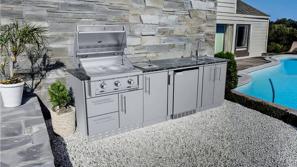 Sunstone Brazos 9ft stainless steel outdoor kitchen island featuring an open Ruby 3-burner grill and sink situated next to a backyard swimming pool and stone wall.
