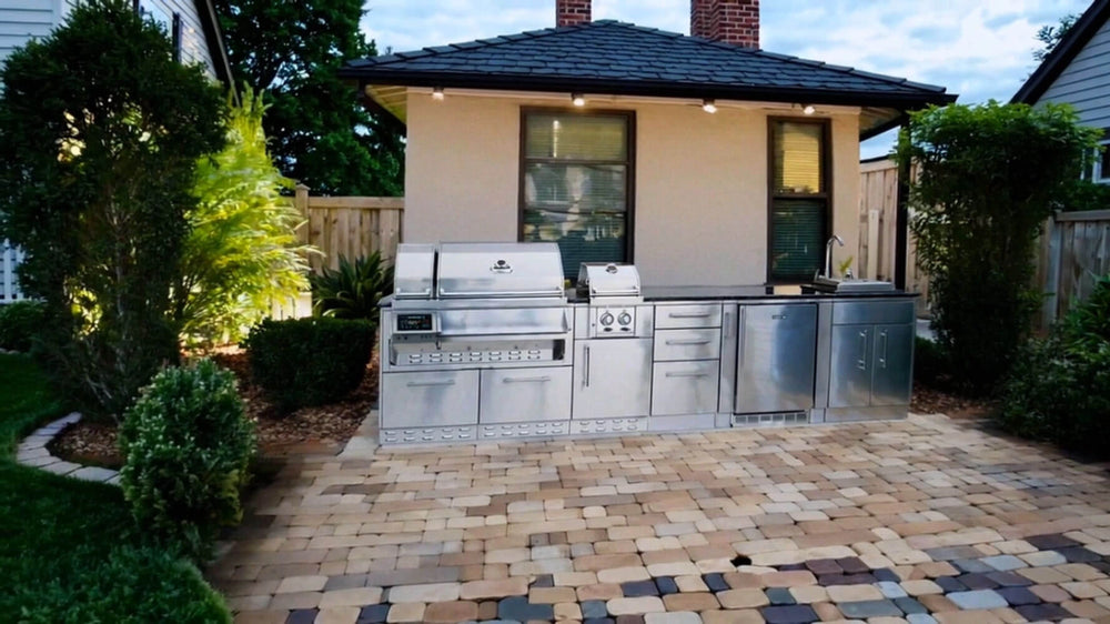 Sunstone SCPCYPRESS11.6 Cypress Outdoor Kitchen Island installed in backyard paver patio, showcasing full stainless kitchen run with grill, side burner, fridge, and sink.