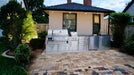 Sunstone SCPCYPRESS11.6 Cypress Outdoor Kitchen Island installed in backyard paver patio, showcasing full stainless kitchen run with grill, side burner, fridge, and sink.