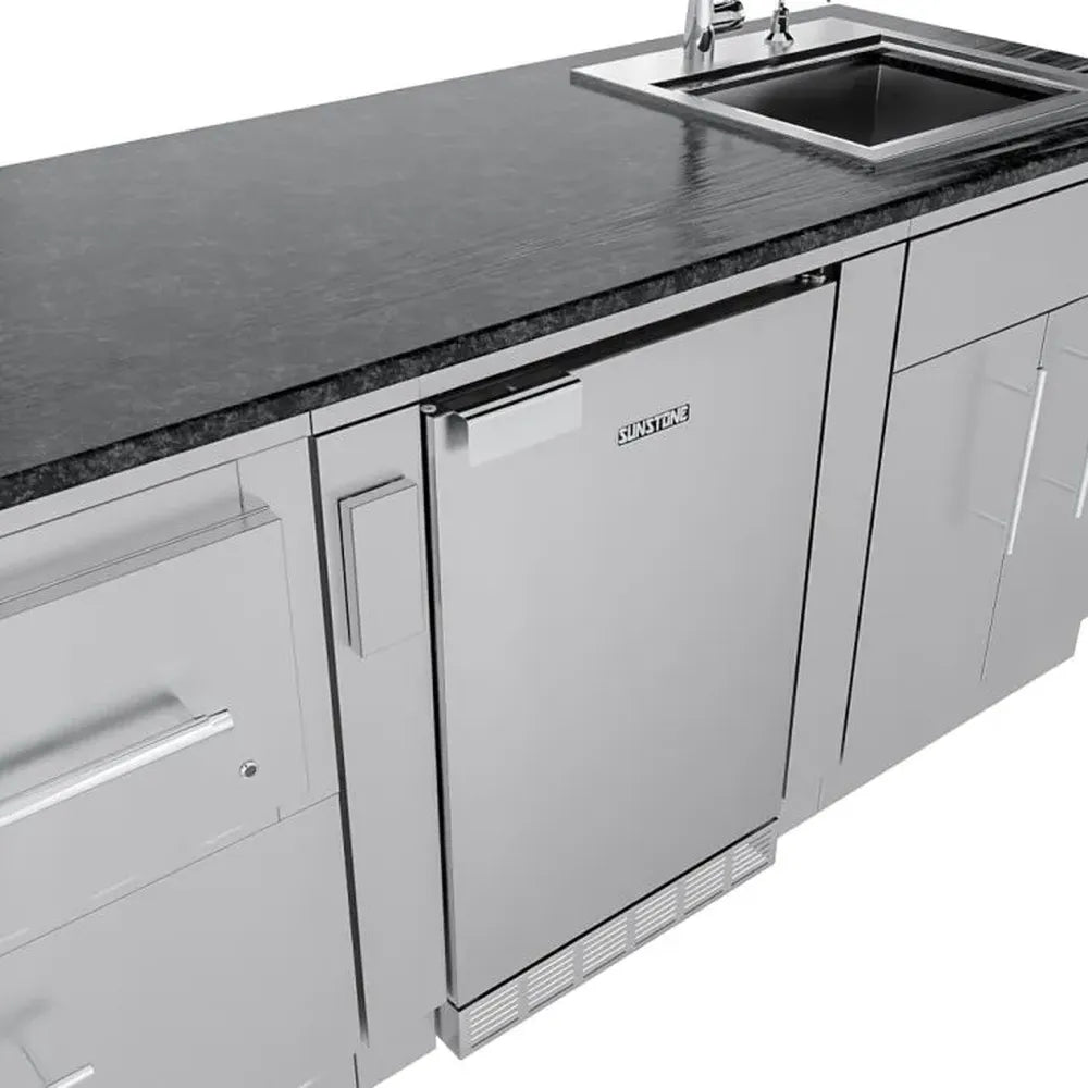 Sunstone SCPFRENCHQUARTER13.7 French Quarter Island under-counter stainless refrigerator next to sink base cabinets beneath black granite.