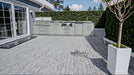 Sunstone Hill Country 13.6 outdoor kitchen island installed on a modern grey paver patio with a lush green privacy hedge background.
