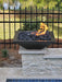 Black Travertine TessaRai 36 inch Square Fire Bowl Kit with lava rock and flame beside fence and waterfront yard