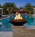 Travertine TessaRai 36 inch Square Fire Bowl Kit glowing at dusk beside luxury swimming pool and tropical landscaping