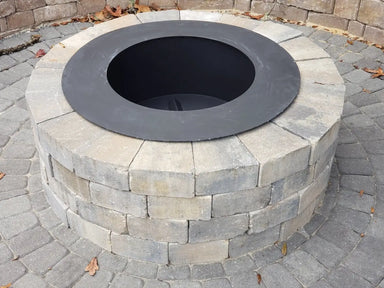 Travertine TessaRai 49-inch smokeless round fire pit with matte black metal insert installed in a tan stone block base.