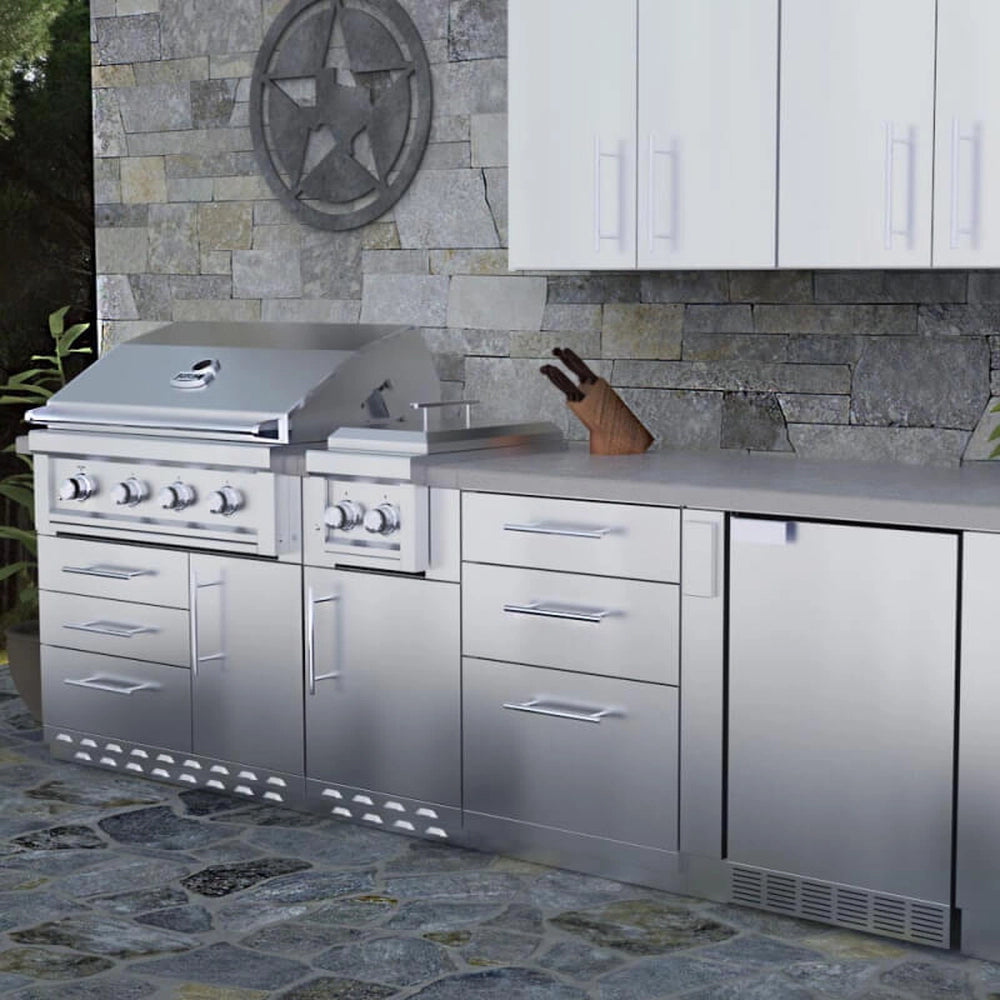 Sunstone SBC24STD 24-inch triple drawer base cabinet installed in a luxury outdoor kitchen island with a stone backsplash, integrated grill, and matching stainless steel cabinetry.