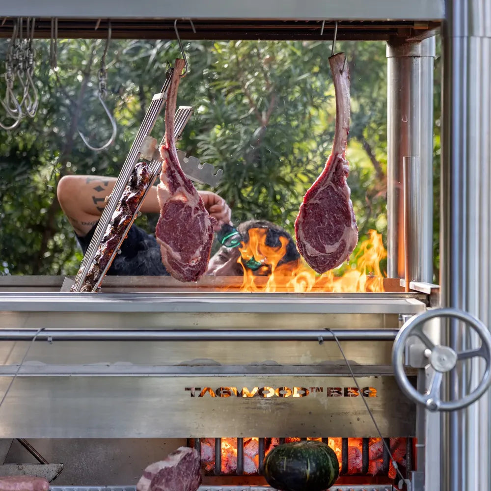 Tagwood BBQ BBQ02SS Santa Maria grill close-up with hanging ribeye steaks over open flame