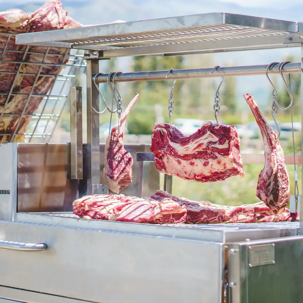 Tagwood BBQ26SS XL Santa Maria grill hanging raw beef cuts on hooks above cooking grates