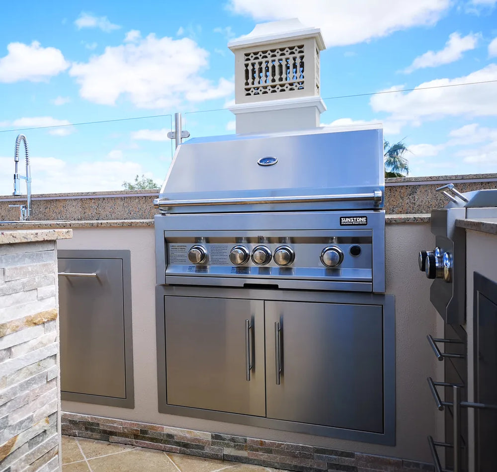 Sunstone 36" stainless double access doors installed below built-in gas grill in outdoor kitchen island with stone countertop.