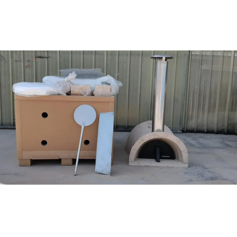 WPPO Tuscany DIY wood-fired oven kit beside shipping crate with chimney, pizza peel, insulation, and assembly materials.