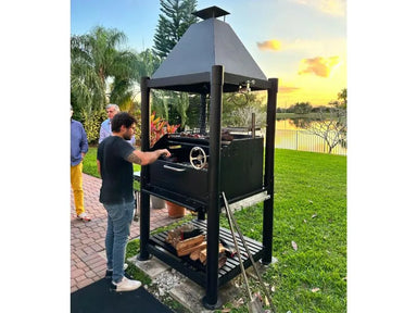 Tagwood BBQ BBQ02SIB Santa Maria grill in backyard setting with open fire cooking at sunset
