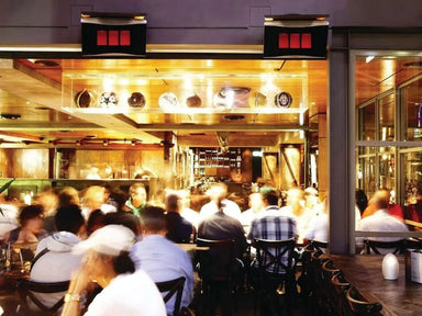 Two Bromic Platinum series heaters mounted above a busy, indoor-outdoor dining area, showing them in use to heat a crowd of people.