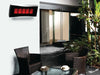 The Bromic Platinum 500 Gas Radiant Heater mounted on a white wall above a residential outdoor patio seating area, with wicker chairs and tropical plants.
