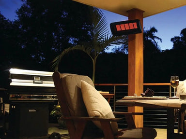 The Bromic Tungsten 300 Gas Radiant Heater mounted on a wooden post on a residential outdoor deck, providing warmth to a seating area with a table and chair.