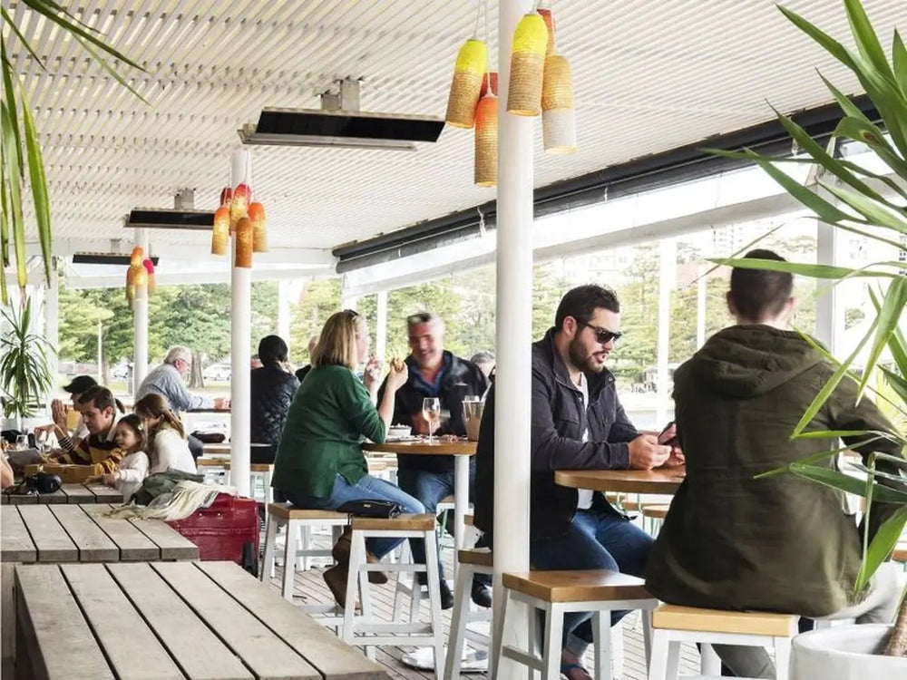 Multiple black Bromic Platinum Electric Heaters mounted on the ceiling of an outdoor restaurant or cafe.
