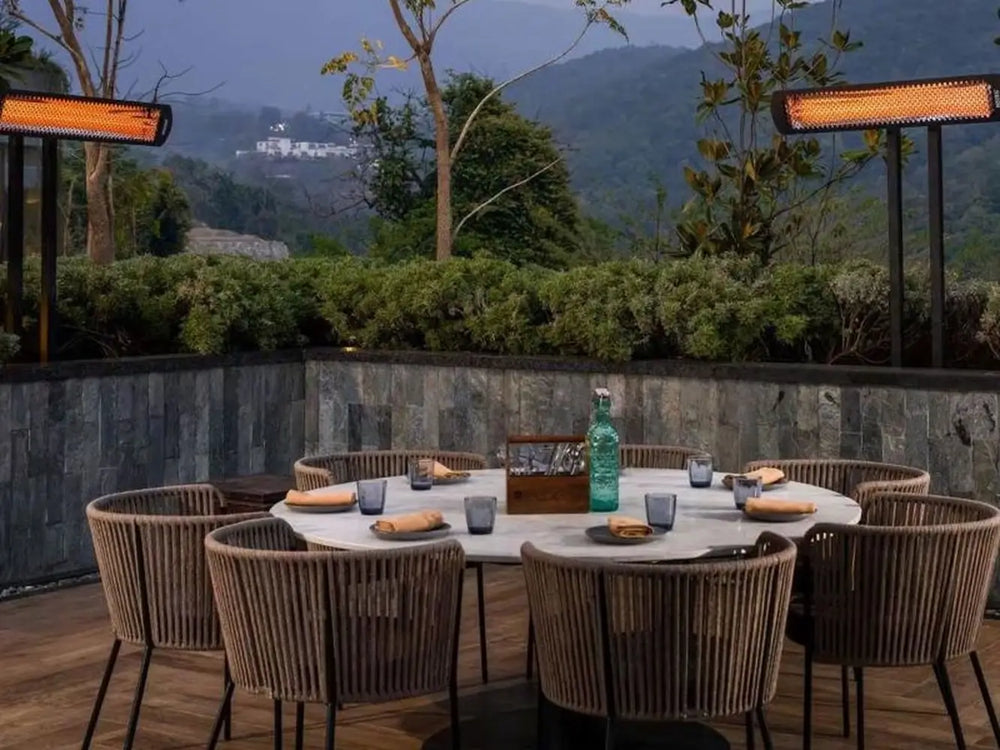 Pair of Bromic Smart-Heat black portable electric heaters warming an outdoor dining table in a garden setting.