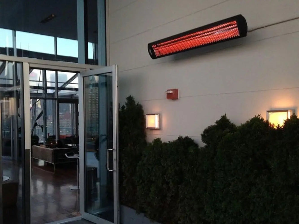 Bromic Tungsten 6000W Electric Heater in black, wall-mounted on a commercial terrace, radiating heat across an urban rooftop lounge.