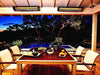 Two Bromic Tungsten 6000W Electric Heaters in black installed above a wooden patio dining area, illuminating a cozy evening meal setup near a pool.