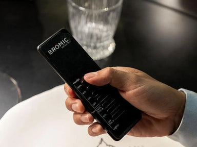 Hand holding the black Bromic Eclipse Dimmer Controller remote, showing 3-stage heat and light adjustment buttons.