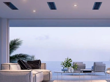 Several Bromic Platinum series electric heaters mounted discreetly on a ceiling of a modern, open-air living space overlooking a beach.