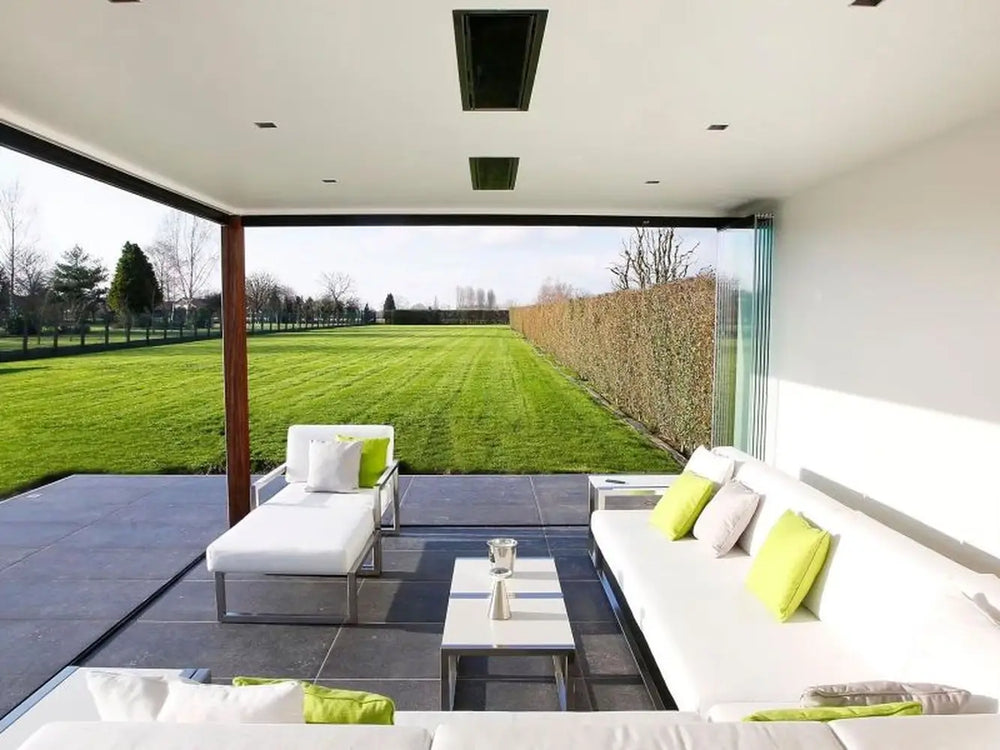 The Bromic Platinum 4500W Electric Heater recessed into a ceiling, blending seamlessly into a luxurious, all-white outdoor lounge area with a large lawn and hedge in the background.