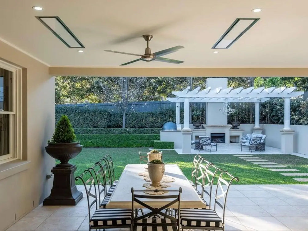 Two Bromic Platinum electric heaters recessed into the ceiling of a modern outdoor patio, providing warmth to a dining and lounge area.