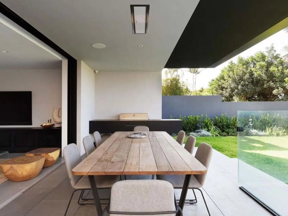 The Bromic Platinum 4500W Electric Heater recessed into a ceiling above an outdoor dining area, adjacent to a built-in grill and a manicured lawn.