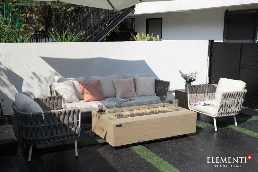 Elementi Plus OFG410SY Colorado 60,000 BTU gas fire table with a handcrafted sunlight yellow stone finish, styled in a luxury poolside outdoor living space with white lounge chairs.