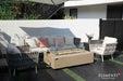 Elementi Plus OFG410SY Colorado 60,000 BTU gas fire table with a handcrafted sunlight yellow stone finish, styled in a luxury poolside outdoor living space with white lounge chairs.