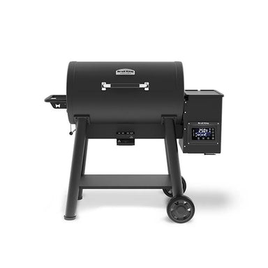 Front view of the Broil King Crown Pellet 500 WiFi pellet smoker in matte black, featuring a barrel-style cooking chamber, chrome handle, side pellet hopper with digital controller, small front shelf, lower support shelf, and two transport wheels on a light gray background.