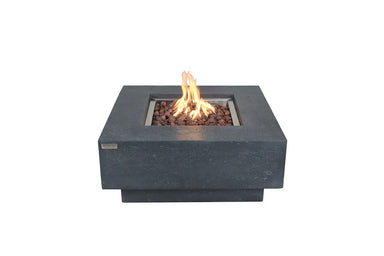 Square Elementi Manhattan fire pit table in dark grey concrete with a center flame and red lava rocks on a white background.