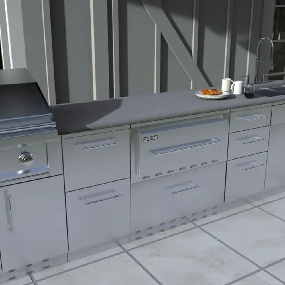 Modern outdoor kitchen island featuring a built-in Sunstone 30-inch warming drawer with a Designer Series face panel, integrated among other stainless steel cabinetry.