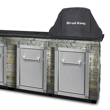 Broil King KA5537 built-in Keg 2000 grill cover shown on a stone outdoor kitchen island with stainless cabinet doors.