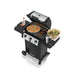 Broil King Gem 310 compact gas grill with lid open, showing cooking grates topped with pizza, burgers, skewers, and salad setup on the side shelves for outdoor grilling