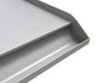Close-up of Sunstone stainless griddle showing front oil/grease reservoir and raised sidewall edge.