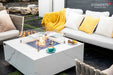 Modern backyard patio scene showcasing the Elementi Plus Bianco rectangular gas fire pit table as a centerpiece for a luxury outdoor lounge area.