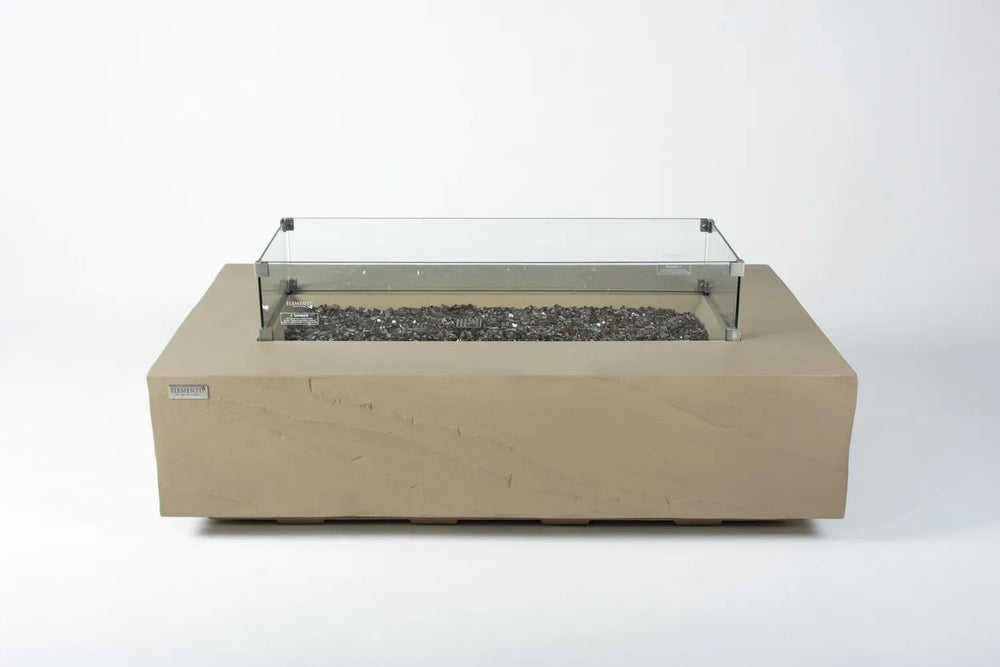 Close-up of the Colorado fire table’s linear burner, showing the clear tempered glass wind guard protecting a warm flame over natural lava rock fire media.