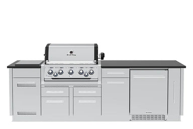 Front view of a Broil King Imperial S 590iF stainless steel outdoor grill island featuring a 5-burner gas grill, built-in storage drawers, and an outdoor refrigerator under a black countertop.