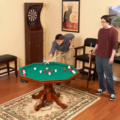 Two men playing bumper pool on an octagonal green felt game table in a home recreation room with a dartboard in the background.