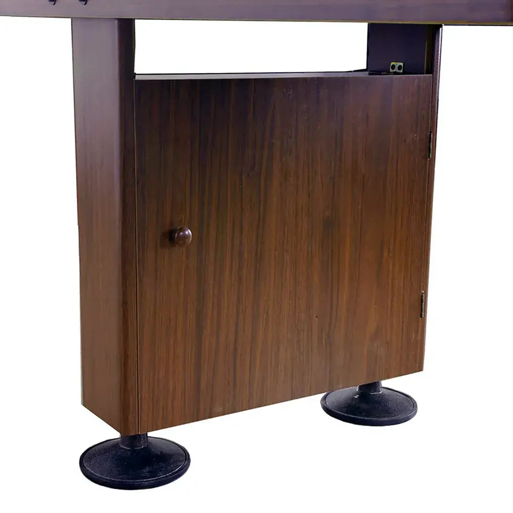 Close-up of a dark wood-finish shuffleboard cabinet leg with a storage compartment door and large black adjustable leg levelers.